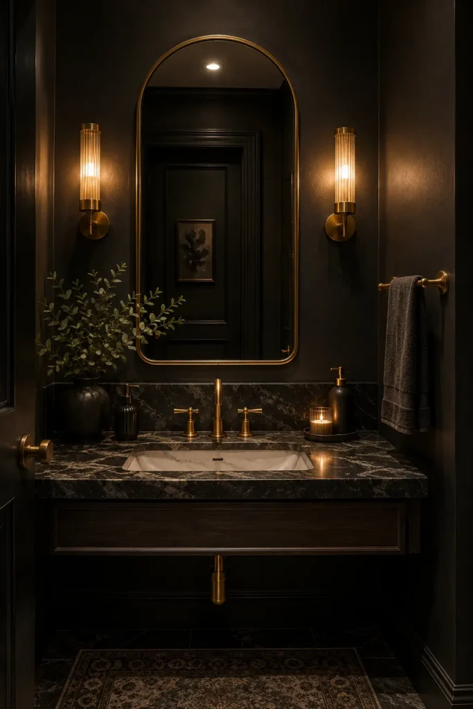 Dark moody bathroom with charcoal walls, brass faucet, gold towel bar, arched mirror, marble sink, and warm ambient lighting.